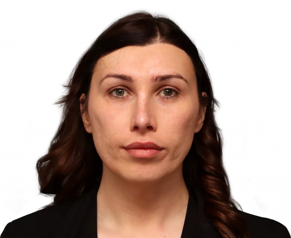 Portrait of a woman facing the camera with dark brown, wavy hair and a neutral expression, wearing a black blazer.