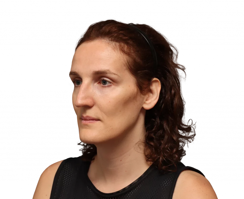 Side profile of a woman with brown curly hair wearing a black sleeveless top and a headband, with a neutral expression.