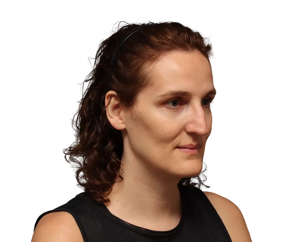 Portrait of a woman with brown curly hair wearing a black sleeveless top, facing right with a neutral expression in a black background