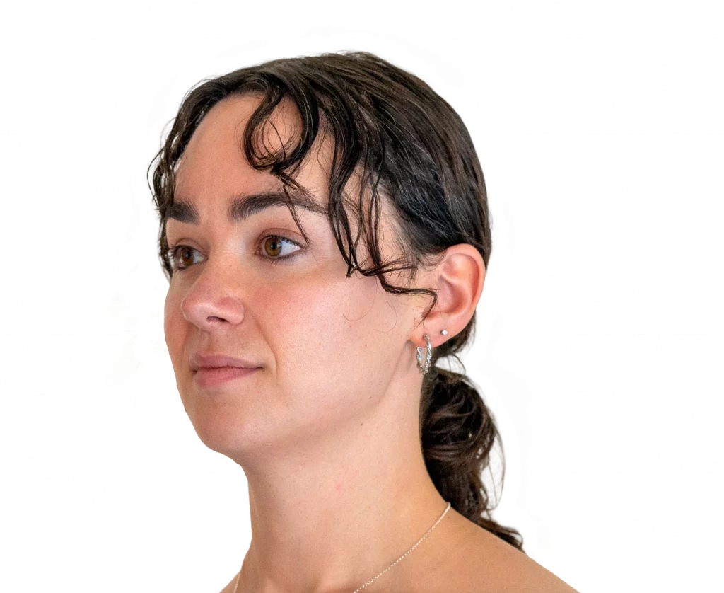 Close-up portrait of a woman with brown hair tied back, looking to the left, wearing small hoop earrings and a delicate necklace.