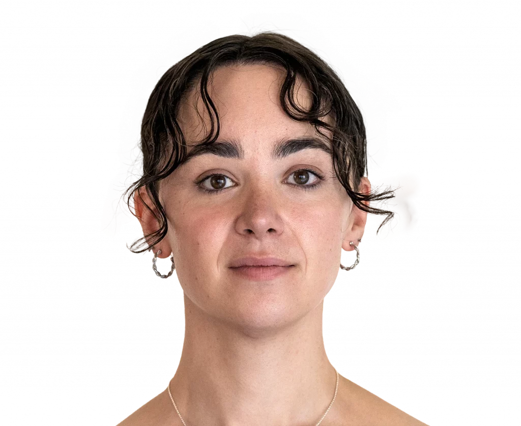 Portrait of a young woman facing the camera with short dark wavy hair, hoop earrings, and a delicate necklace.