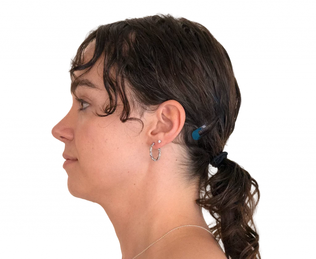 Side profile of a woman with dark hair tied in a ponytail, wearing a silver hoop earring and a blue hair clip along the back of her head.