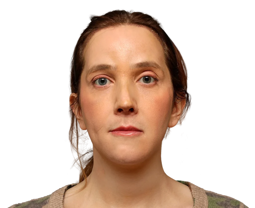 Close-up portrait of a woman facing the camera with light skin, brown hair, and blue eyes, wearing a camouflage sweater against a black background, neutral expression.
