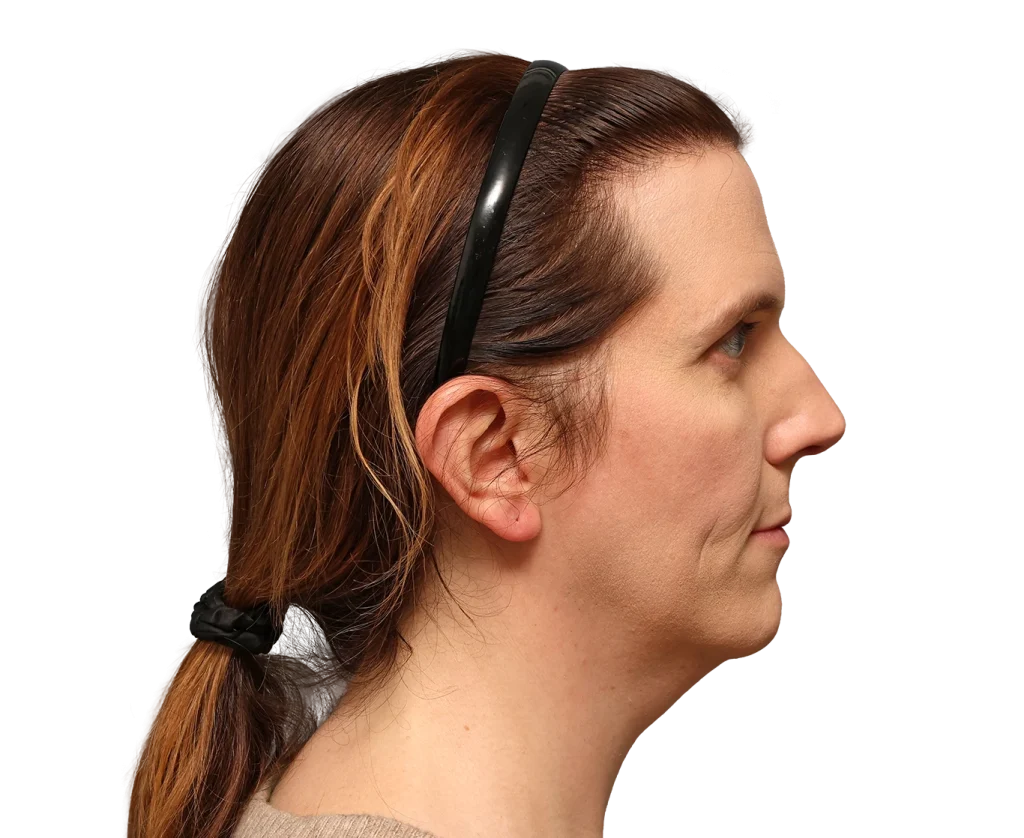 Side profile of a woman with brown hair pulled back in a low ponytail, wearing a black headband against a neutral background.