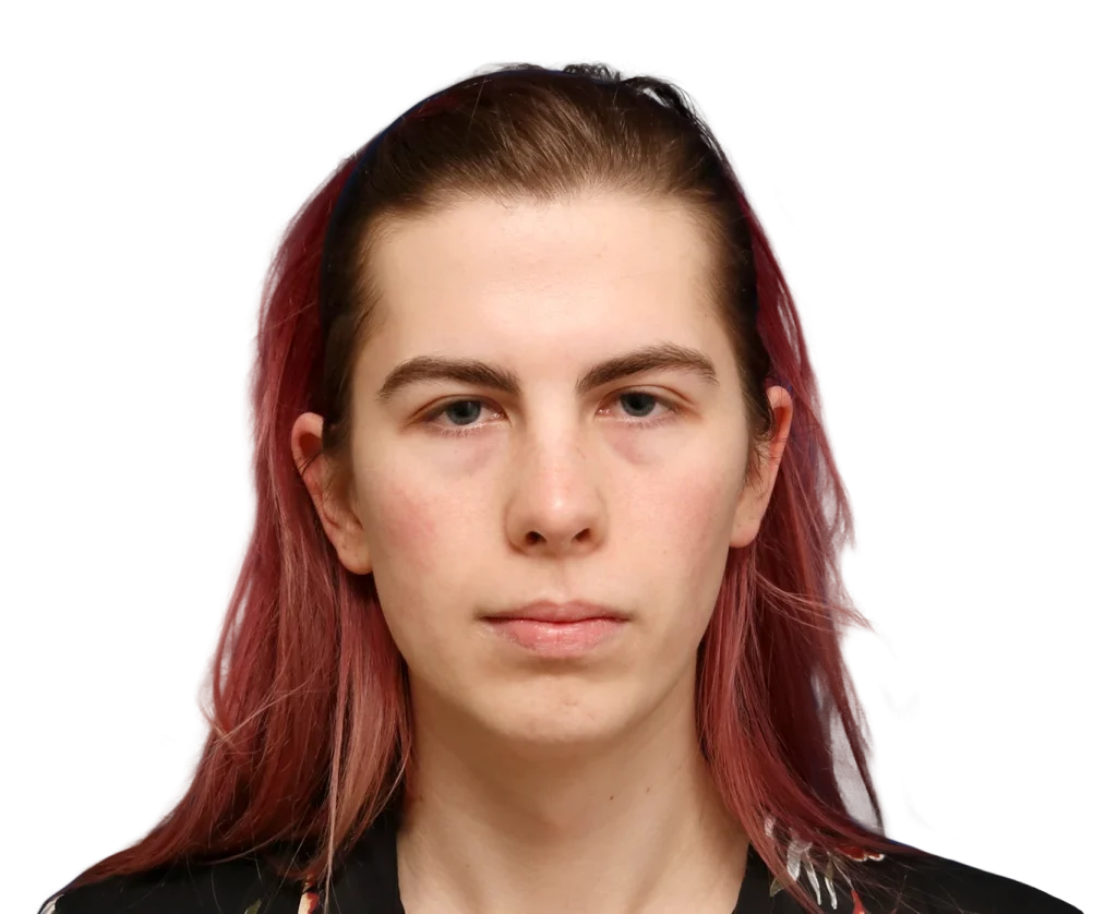 Front-facing head-and-shoulders portrait of a person with reddish-pink hair and a neutral expression against a black background