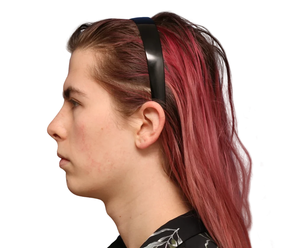Profile view of a person with pink-dyed hair wearing black over-ear headphones, facing left
