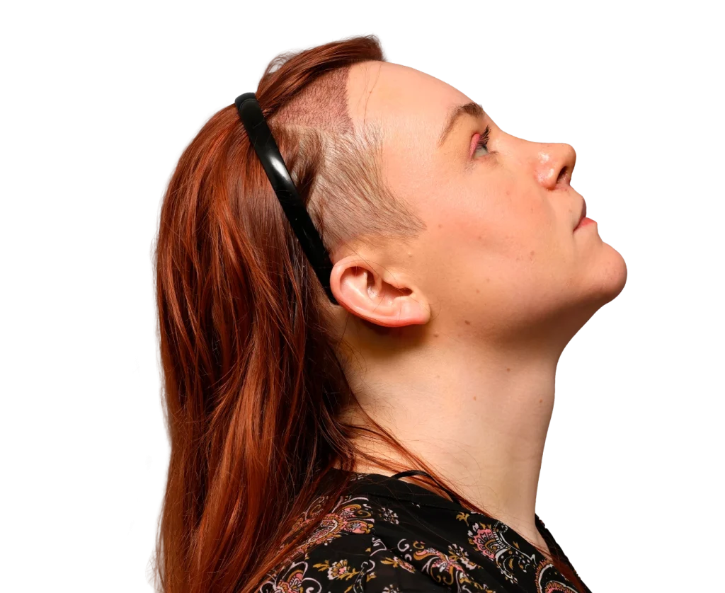 Profile of a person with red hair and an undercut, wearing a black headband, looking upward to the right.