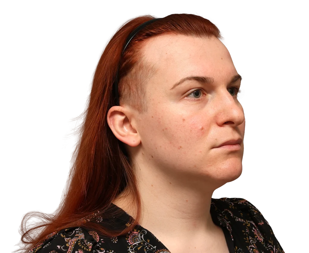 Side profile of a woman with red hair wearing a black headband, neutral expression, and a patterned blouse.