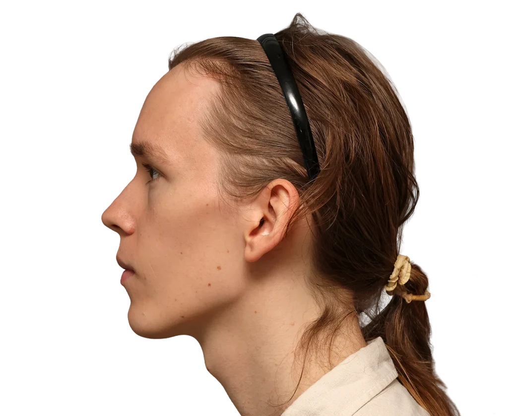 Side profile of a woman with brown hair tied in a low ponytail, wearing a black headband