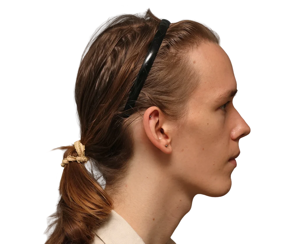 Side profile of a young woman with brown hair tied in a low ponytail and black sunglasses resting on her head.